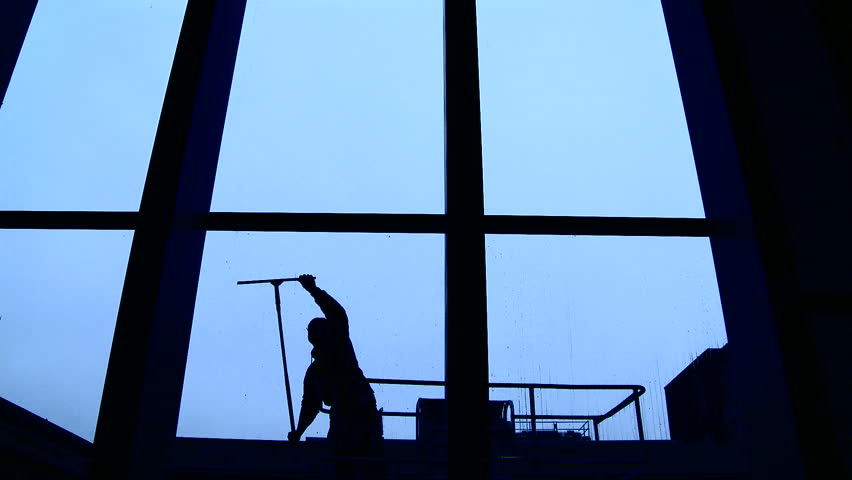 Silhouette of a window cleaner at work in a building with very tall windows.