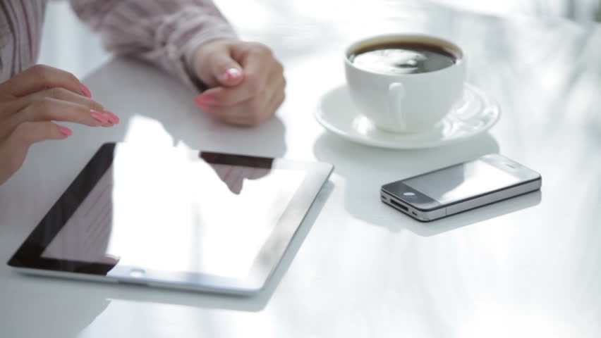 Attractive young woman using touchpad at table and smiling at camera
