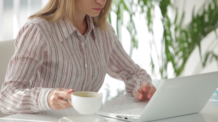 Pretty young woman drinking coffee and working on laptop at office
