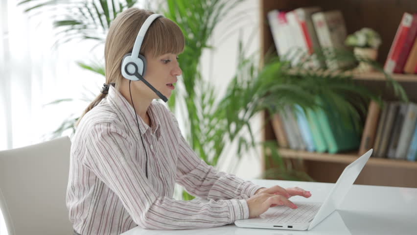Attractive woman in headset sitting at table and working on laptop
