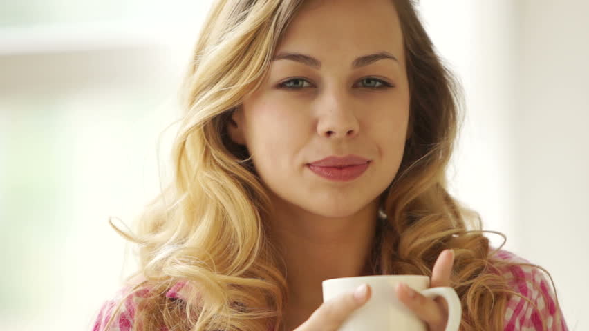 Cute blond girl holding cup of drink and smiling at camera
