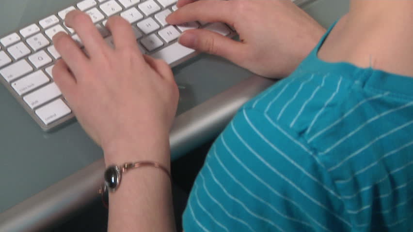 over the shoulder of a woman as she types on a modern computer keyboard on a