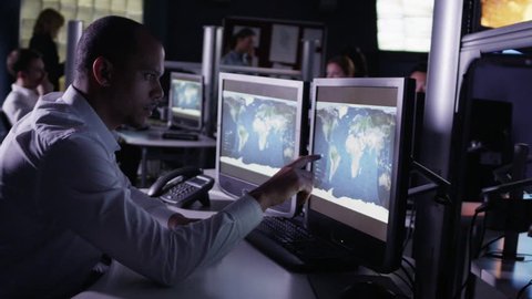 Team of security personnel watching the screens in a system control center. This could be a weather station or airport traffic control room. It could be a police or government surveillance facility.