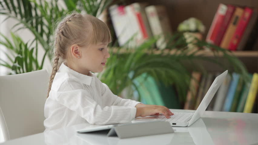 Cute little girl sitting at table with laptop turning around and smiling at