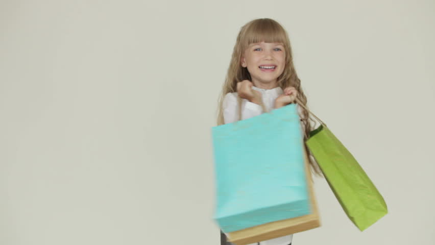 Cheerful funny little girl standing with multicolored paper bags in her hands