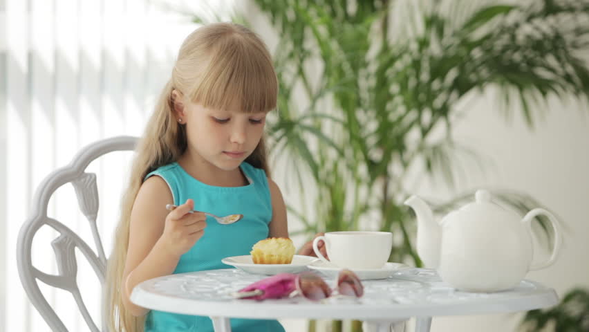 Cute little girl sitting at table eating cake and smiling at camera
