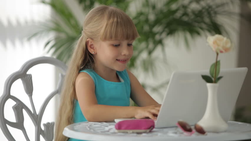 Cute little girl siting at table using laptop opening her wallet and taking out