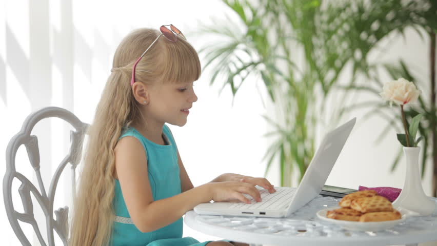 Beautiful little girl sitting at table with laptop showing thumb up and smiling