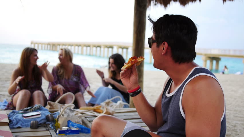 A group of friends gather on the beach and eat pizza.