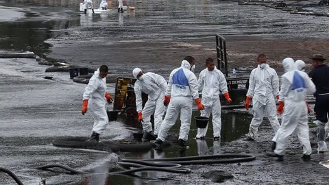RAYONG, THAILAND - JULY 31, 2013: Workers wearing biohazard suits pass a pail full of spilled crude oil as cleaning operations from a beach of Samet Island on July 31, 2013 in Rayong, Thailand.