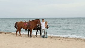 Young couple with horses walking along the beach.