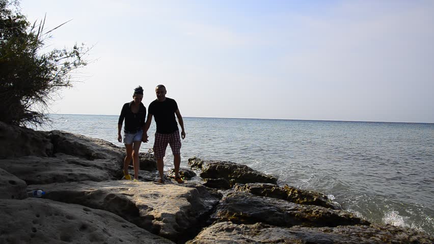 Silhouette walking of romantic couple walking on ocean beach rocks pointing