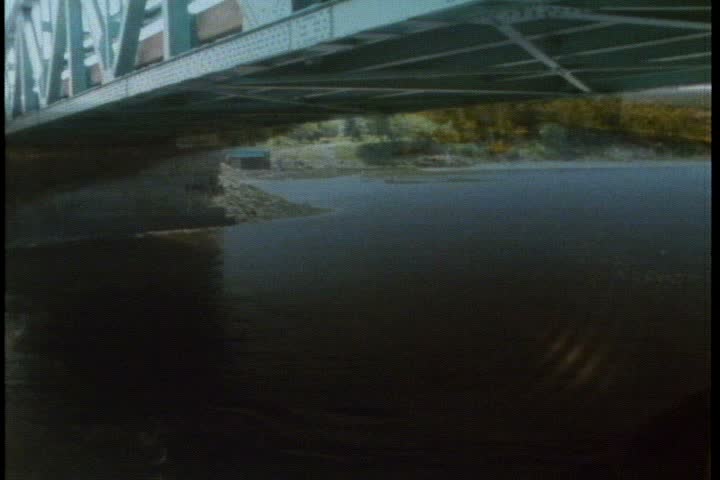 MS flooded river flows under bridge in New England. Camera pans left following the flow of the water.