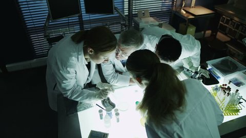 A mature male scientist or medical researcher is working in a dark laboratory, teaching a young team of students or trainees. 