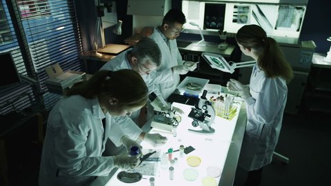 A mature male scientist or medical researcher is working in a dark laboratory, teaching a young team of students or trainees. 