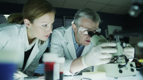 A mature male scientist or medical researcher is working in a dark laboratory, teaching a young female student or trainee. 