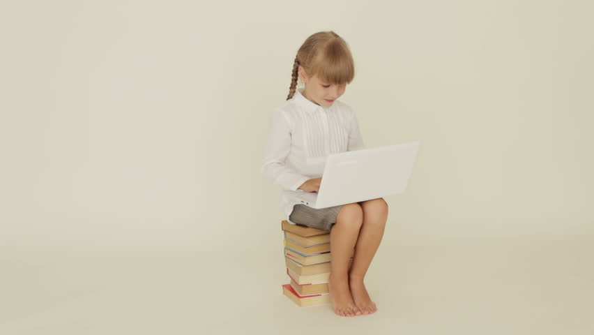 Pretty little girl sitting on stack of books using laptop showing thumb up and