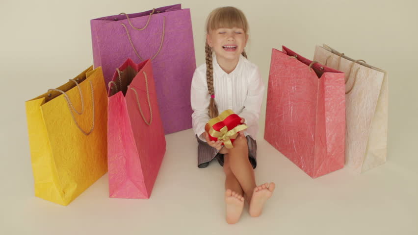 Funny little girl sitting on floor surrounded by shopping bags holding