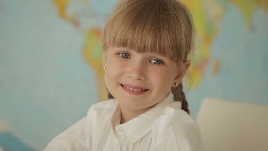 Pretty little girl sitting at desk using laptop and smiling at camera