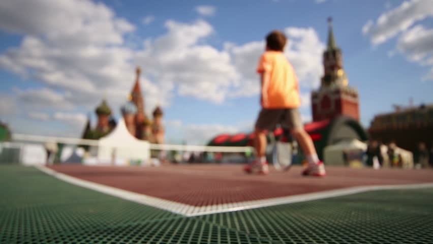 Young boy plays tennis on Red square near Kremlin in Moscow, (unfocused)