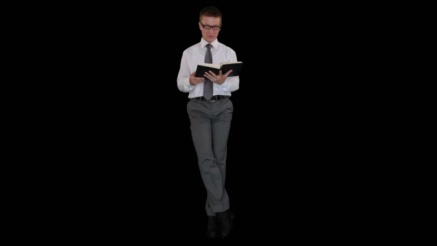 Young businessman with glasses reading a book and sitting, against black