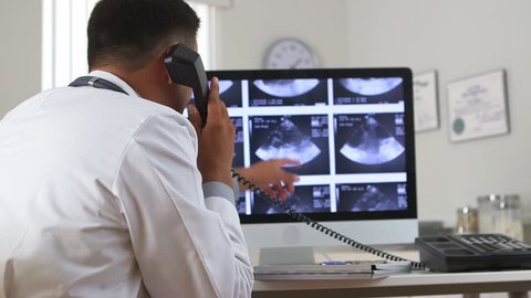 Mexican doctor viewing sonogram on computer while talking on phone