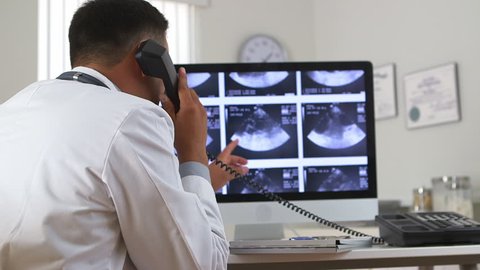 Latino doctor viewing sonogram on computer while talking on phone