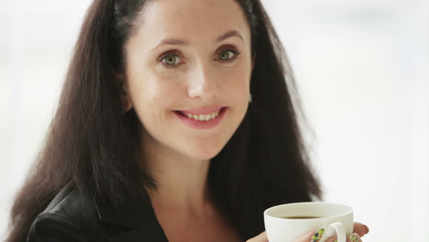 Attractive young woman enjoying coffee smiling and looking at camera