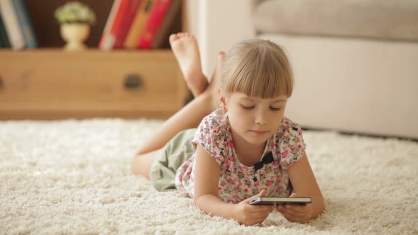 Pretty little girl lying on floor with mobile phone looking at camera and