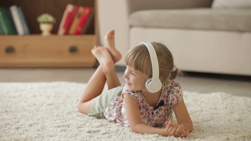 Funny little girl lying on floor listening to music in headset smiling and