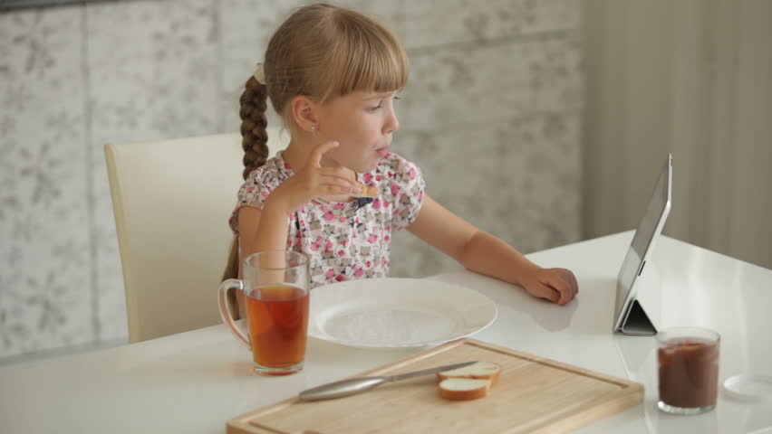 Pretty little girl at kitchen eating chocolate sandwich drinking juice and using