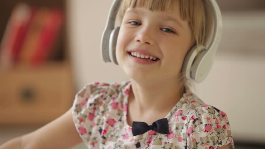 Pretty little girl in headphones waving her hand and smiling at camera