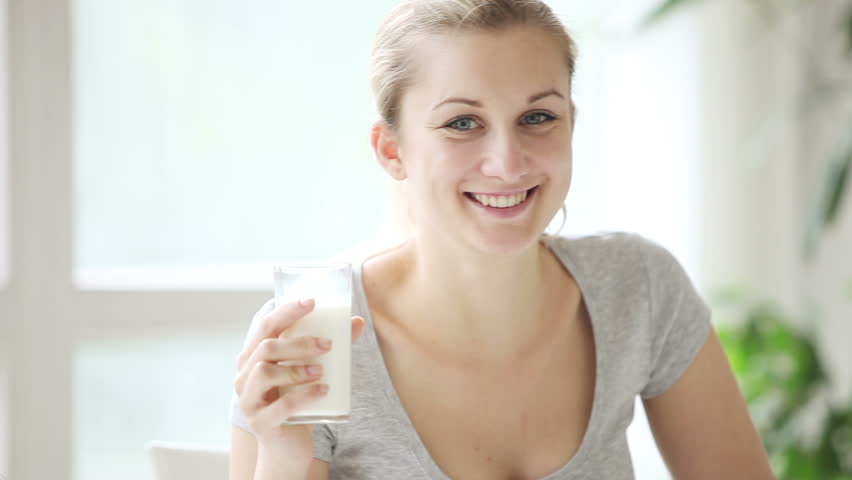 Attractive young woman sitting at table smiling at camera and drinking milk from