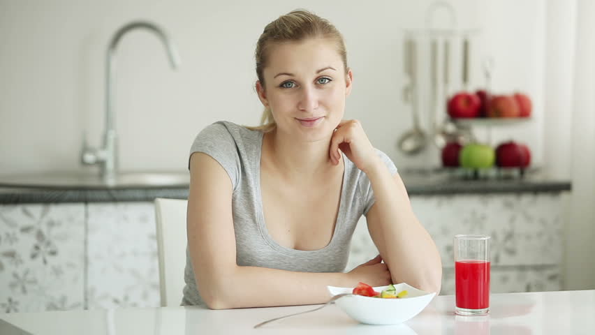 Attractive young woman sitting at kitchen table with bowl of vegetable salad and