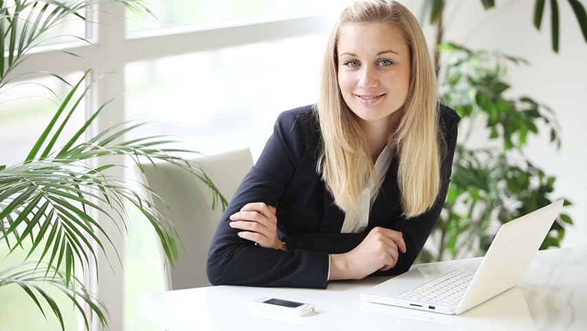 Attractive formaly dressed young woman using laptop and smiling at camera