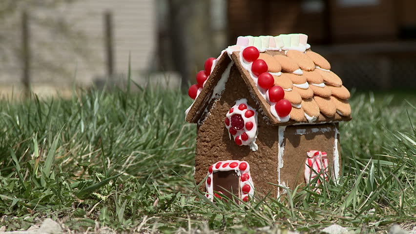 Gingerbread house is stomped flat by a booted foot.  Street with cars passing in