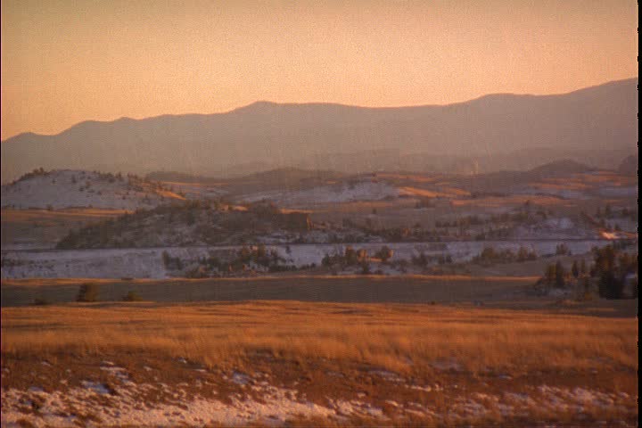 WS grassy Wyoming prairie with light snow cover, camera pans right. Mountains on the horizon in background in Laramie, Wyoming.
