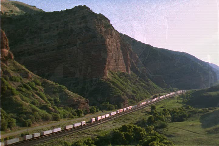 WS freight train moves past tall green mountains in Laramie, Wyoming.