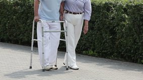 Male retiree doing step after step with a walker, his wife supporting him