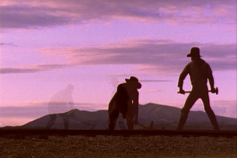 Historical reenactment in Promontory, Utah. MS two workers in silhouette pounding railroad spikes with sledgehammers under a purple sunset.