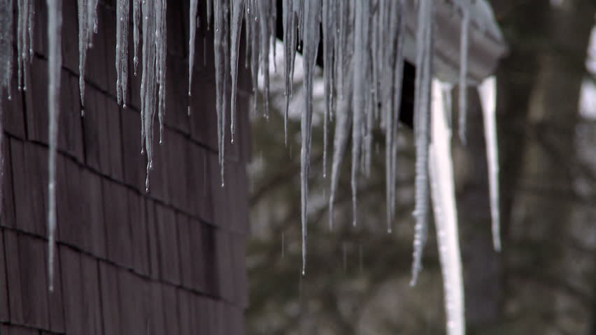Row of icicles hanging off a roof, dripping.