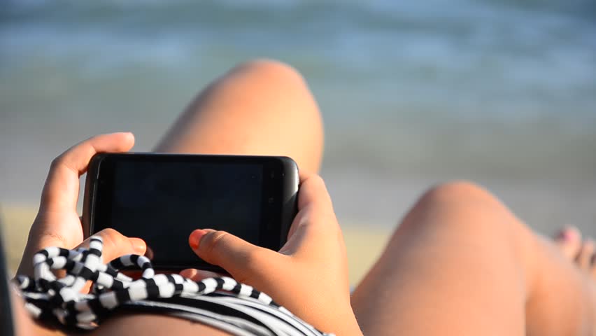 Woman using smartphone while sunbathing on beach close up