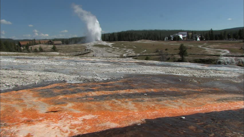 Water runs over a rock shale surface with geyser and observation deck in the
