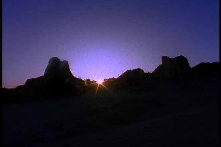 Bright ball of sun rises behind silhouette of jagged hills in Australia.