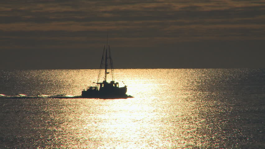 Fishing boat passes across a sea backlit by the rising sun