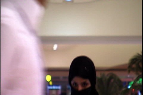 RIYADH, SAUDI ARABIA - SEPTEMBER 25, 2002: Woman in black niqab using cell phone as she gets off the escalator.