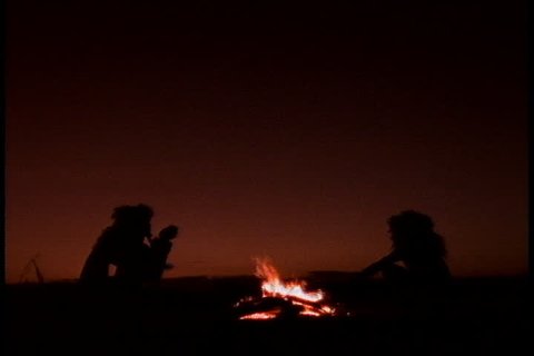 Historical reenactment in East Africa. Silhouettes of family of early humans, or Homo erectus, sitting around a camp fire.