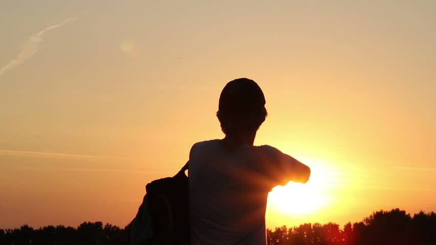Tired traveler enjoys dusk, takes off backpack and cap