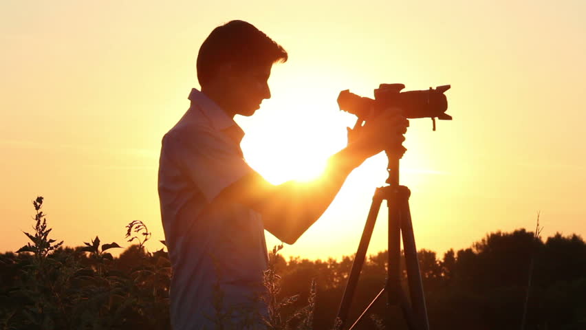 Young man shooting photo video in dusk dawn sun, camera