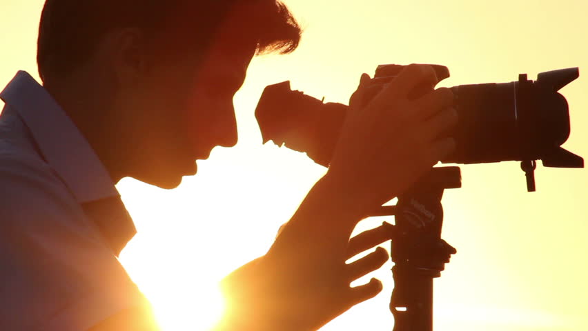 Camera on tripod, young cameraman shoots photos and videos, dusk